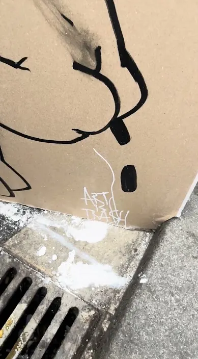 Cardboard drawing above a drain – urban art by Art Is Trash Drawn cardboard leaning above a drain grate on the street, Barcelona, Art Is Trash