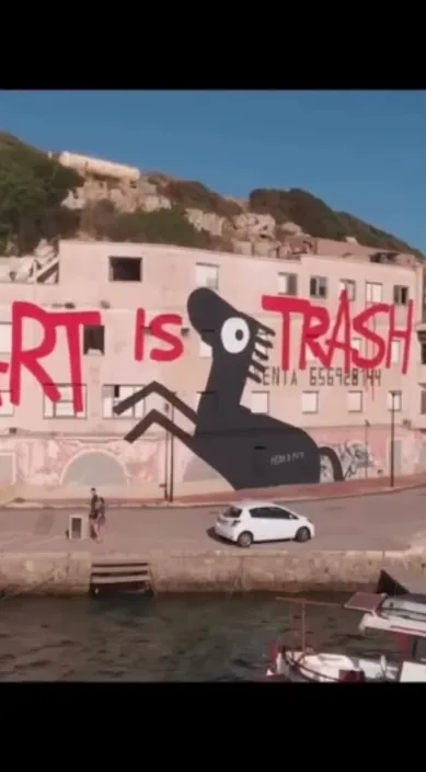 Large Art Is Trash mural with a black figure on a white wall beside the water